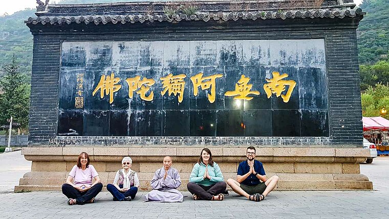Touristen vor einem Denkmal in China im Schneidersitz mit einem Mönch