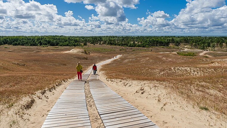 2 Leute laufen auf einem Steg in der Dünenlandschaft des Baltikums
