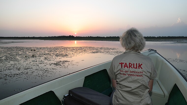 Frau sitzt im Boot und beobachtet den Sonnenuntergang im Donaudelta in Rumänien