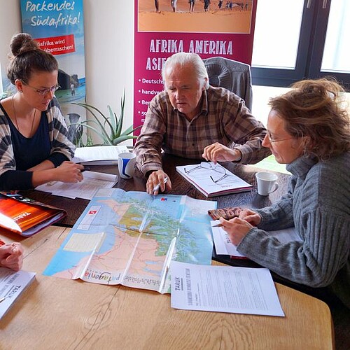 Drei Menschen am Tisch planen Reiserouten