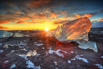 Das rote Licht des Sonnenuntergangs bricht durch die kristallenen Eisstücken am Diamond Beach in Island