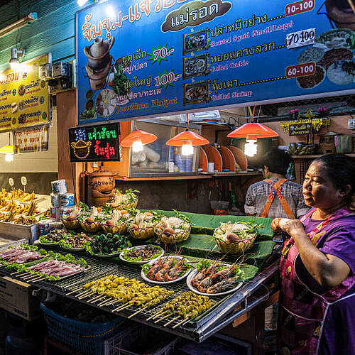 Frau steht an einem Marktstand mit Streefood in der Nacht in Thailand