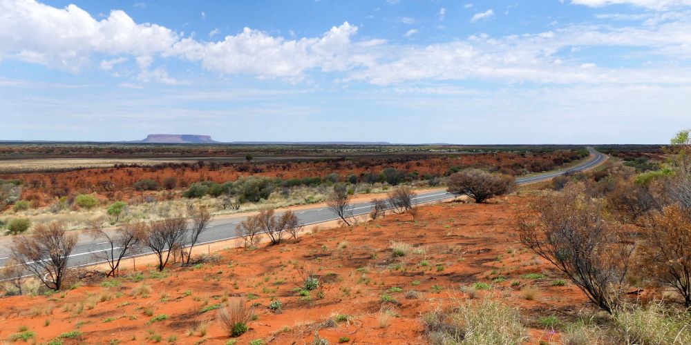 Straße durch das Outback mit dem Uluru / Ayers Rock im Hintergrund in Australien