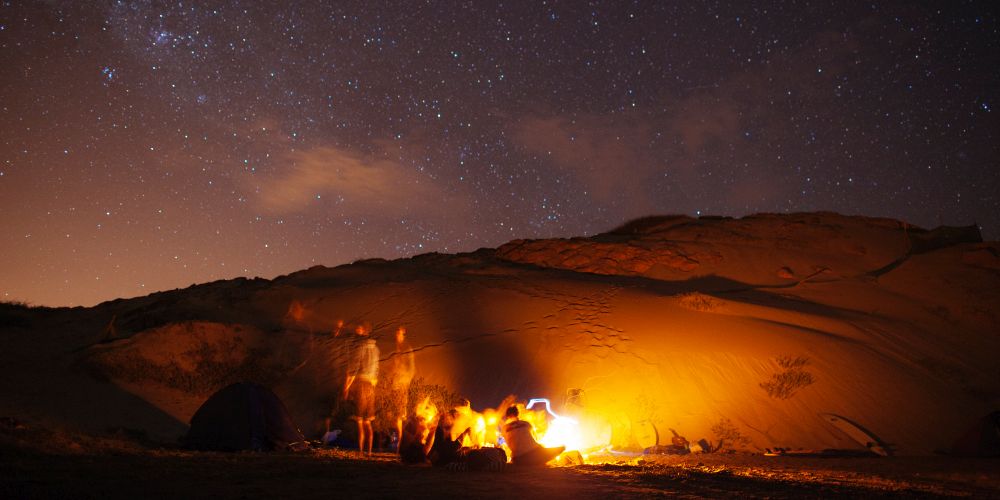 Menschen am Lagerfeuer in der Wüste unter Sternenhimmel