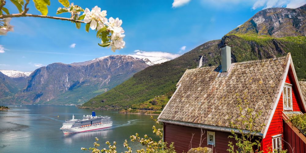 Rotes Haus am Geirangerfjord mit Kreuzfahtschiff in Norwegen