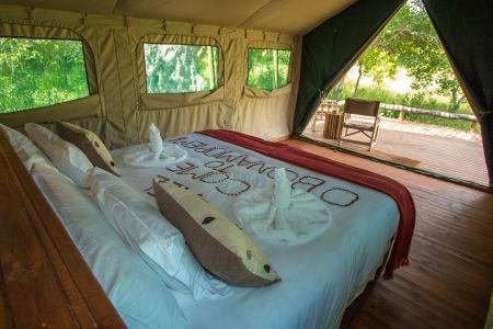 Bett mit Schlafzimmer und Holzdeck in der O Bona Moremi Safari Lodge