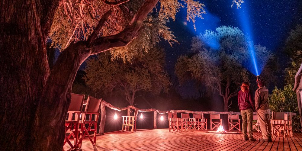 2 Personen schauen in den Sternenhimmel auf dem Holzdeck der O Bona Moremi Safari Lodge