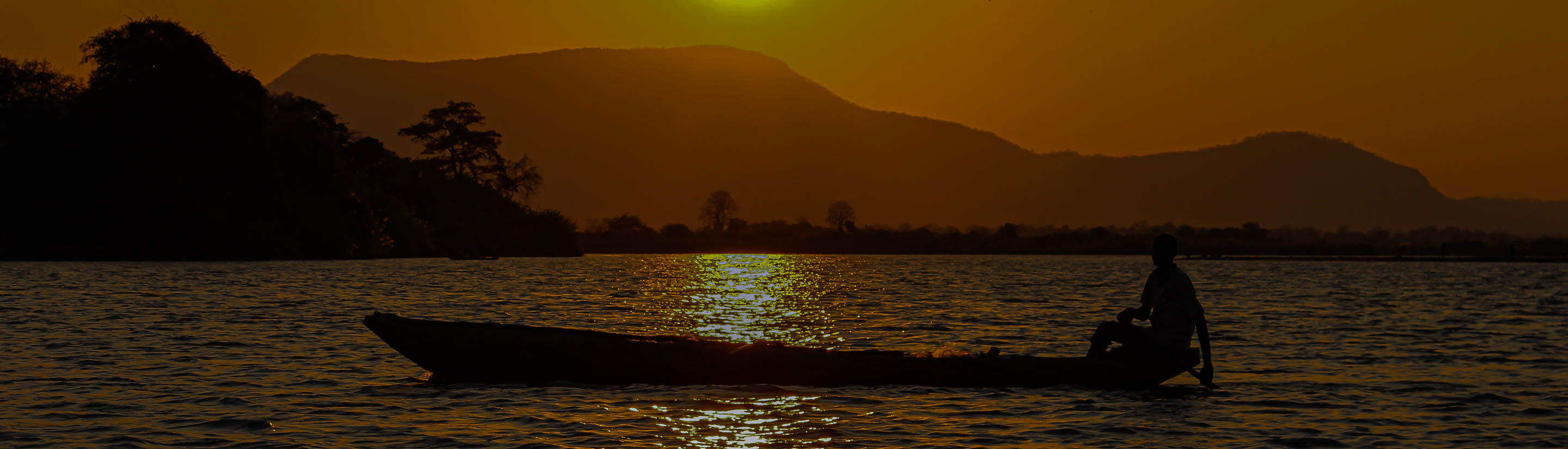 Mann im Einbaumboot auf See im Sonnenuntergang in Malawi.