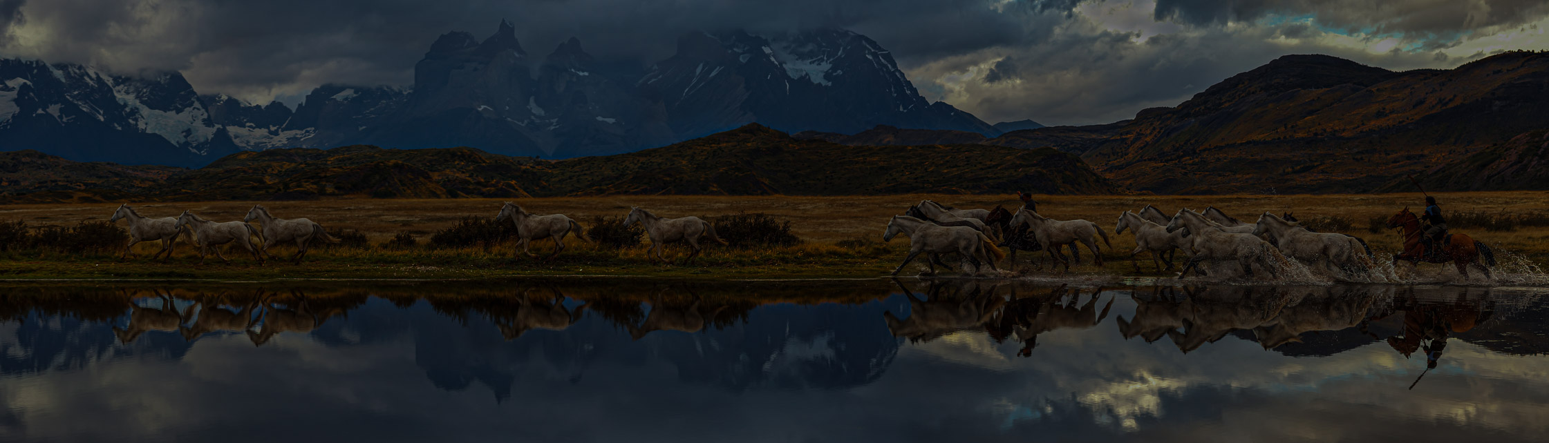 Gaucho treibt eine Herde Pferde vor einem See im Torres del Paine Nationalpark in Amerika