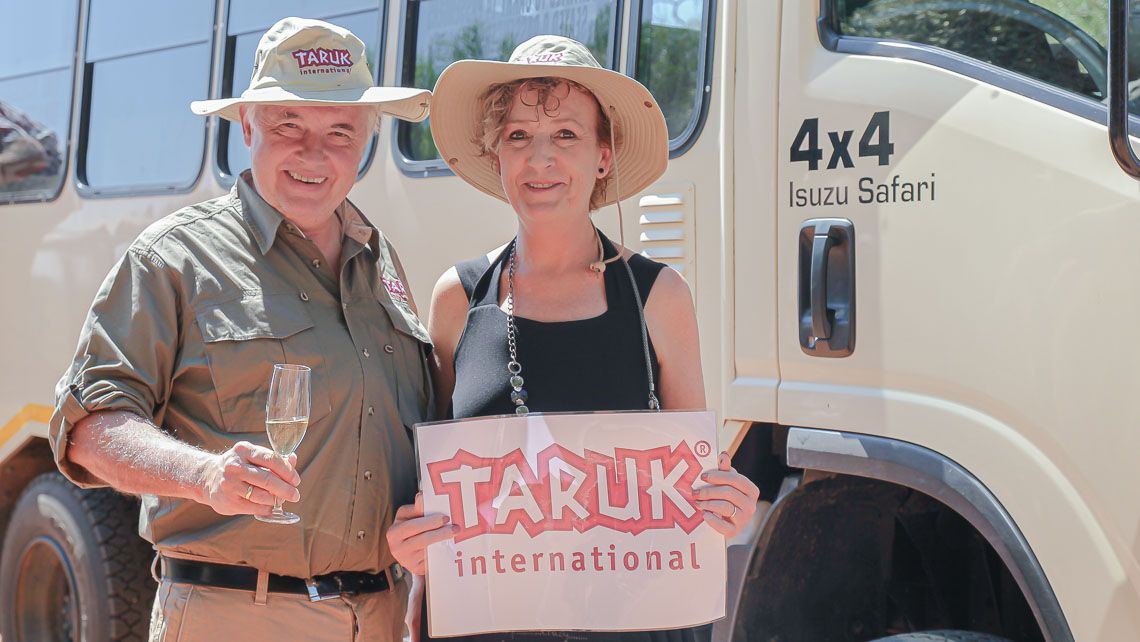 Ehepaar mit Sekt und Schild vor Geländewagen